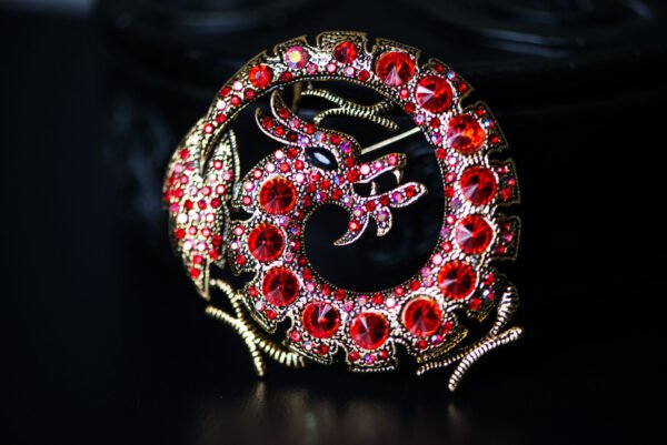 Broche dragon ornée de strass, mesurant 5,3 cm x 2,8 cm. Symbole de puissance et de sagesse, ce bijou élégant brille de mille feux, ajoutant une touche mystique à votre tenue. Léger (30 g) et polyvalent, il s'adapte à toutes les occasions, des événements formels aux sorties décontractées. Un accessoire unique qui évoque les légendes anciennes et affirme votre style audacieux.